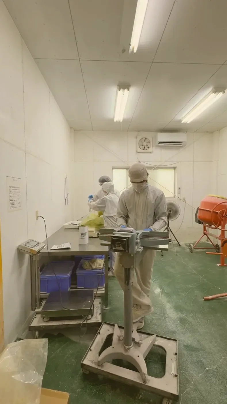 The packing room at the Osaki-cho factory: staff in food-grade whites at the steel table, the bench sealer and mixer stationed around them