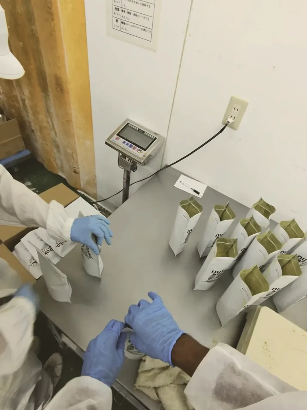 Rows of filled Nutroko pouches standing open on the steel table, waiting to be weighed and sealed