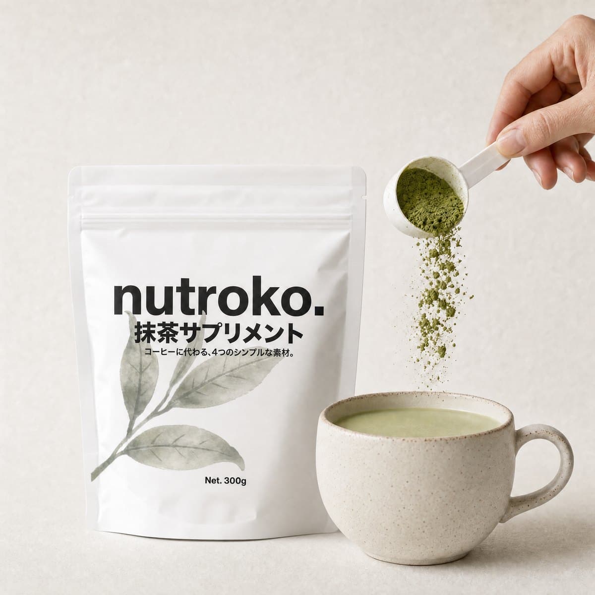 Nutroko pouch beside a stoneware mug of the prepared matcha supplement, a hand tipping a scoop of green powder above the mug