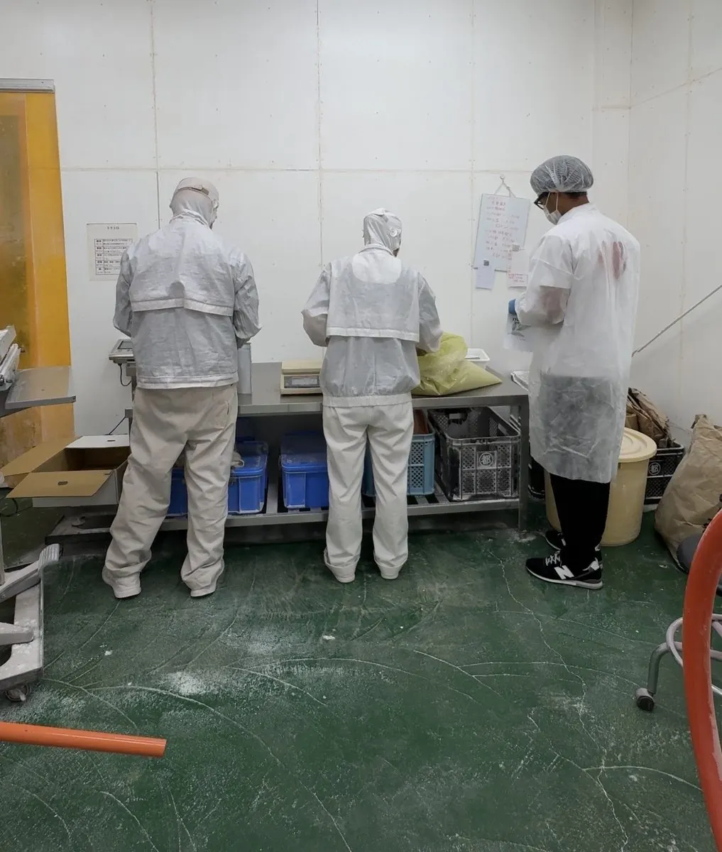 大崎町のさつまいも工場で、白衣姿でパウチを量って封をする南海と2人のスタッフ